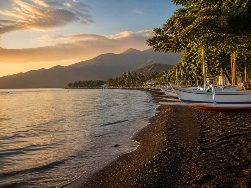Black sand beach and traditional fishing boats at Pemuteran bay, West Bali, at sunset