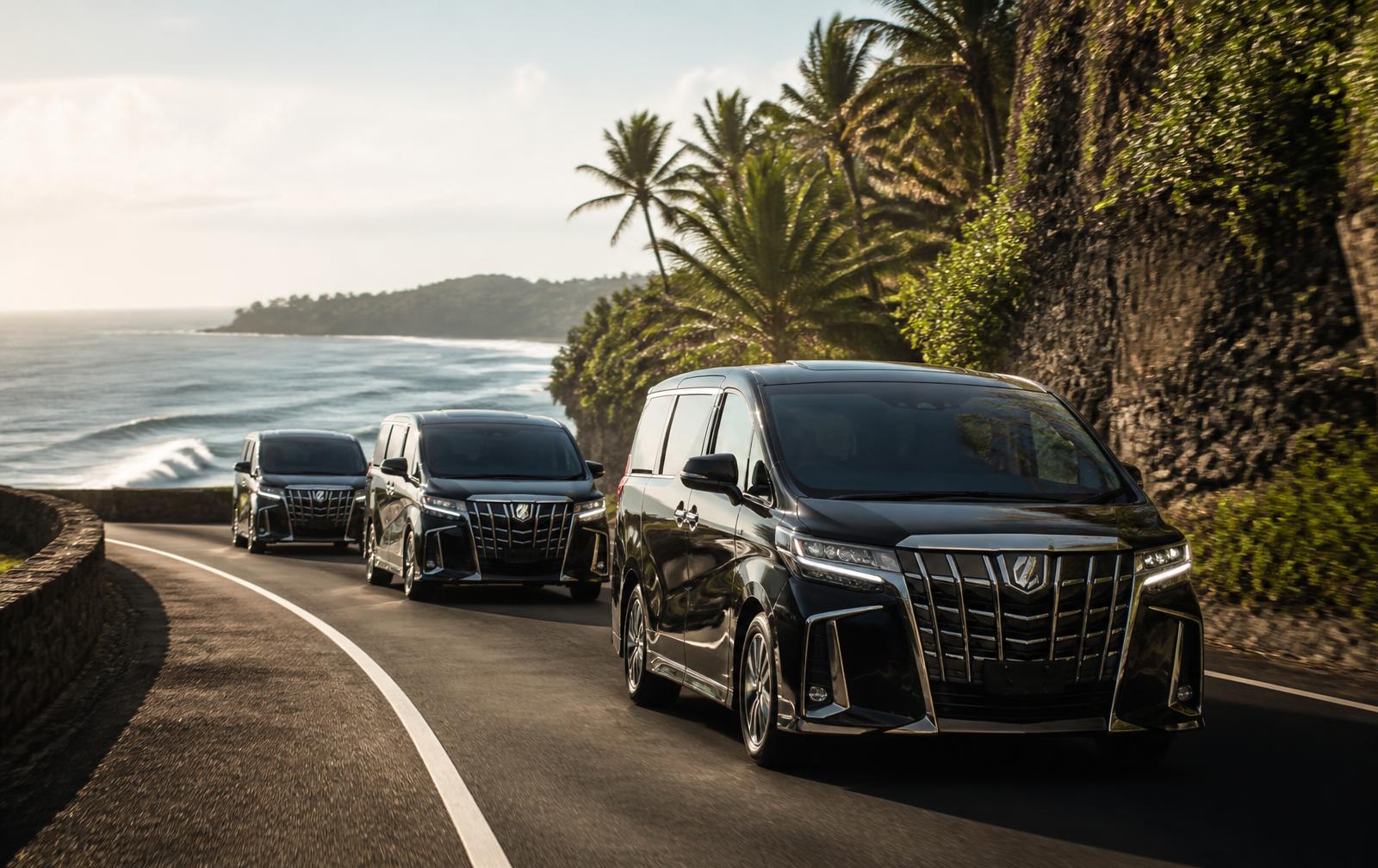 Convoy of black premium vans travelling along a Bali coastal road for a group transfer